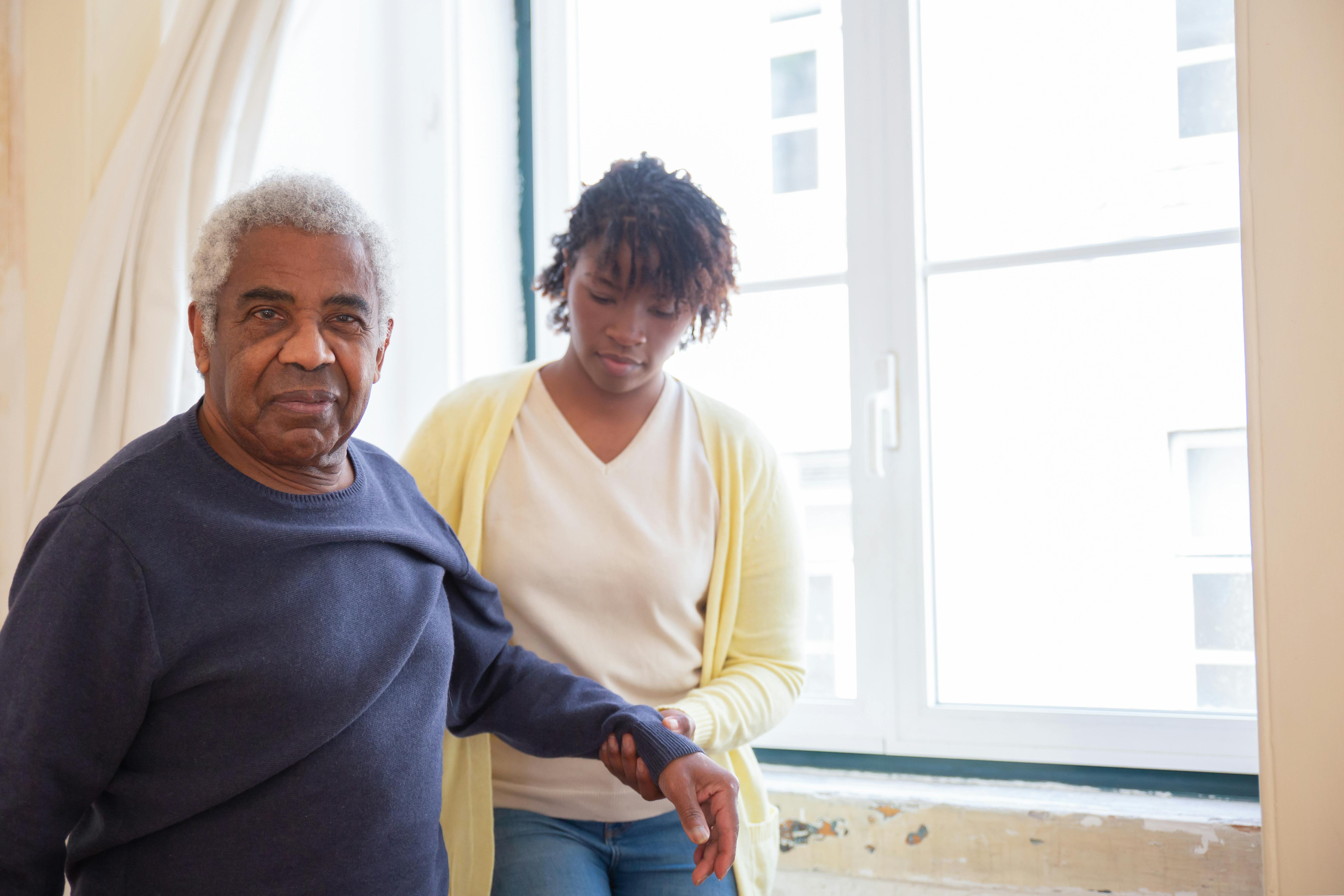 Caregiver gently assisting elderly man with mobility at home
