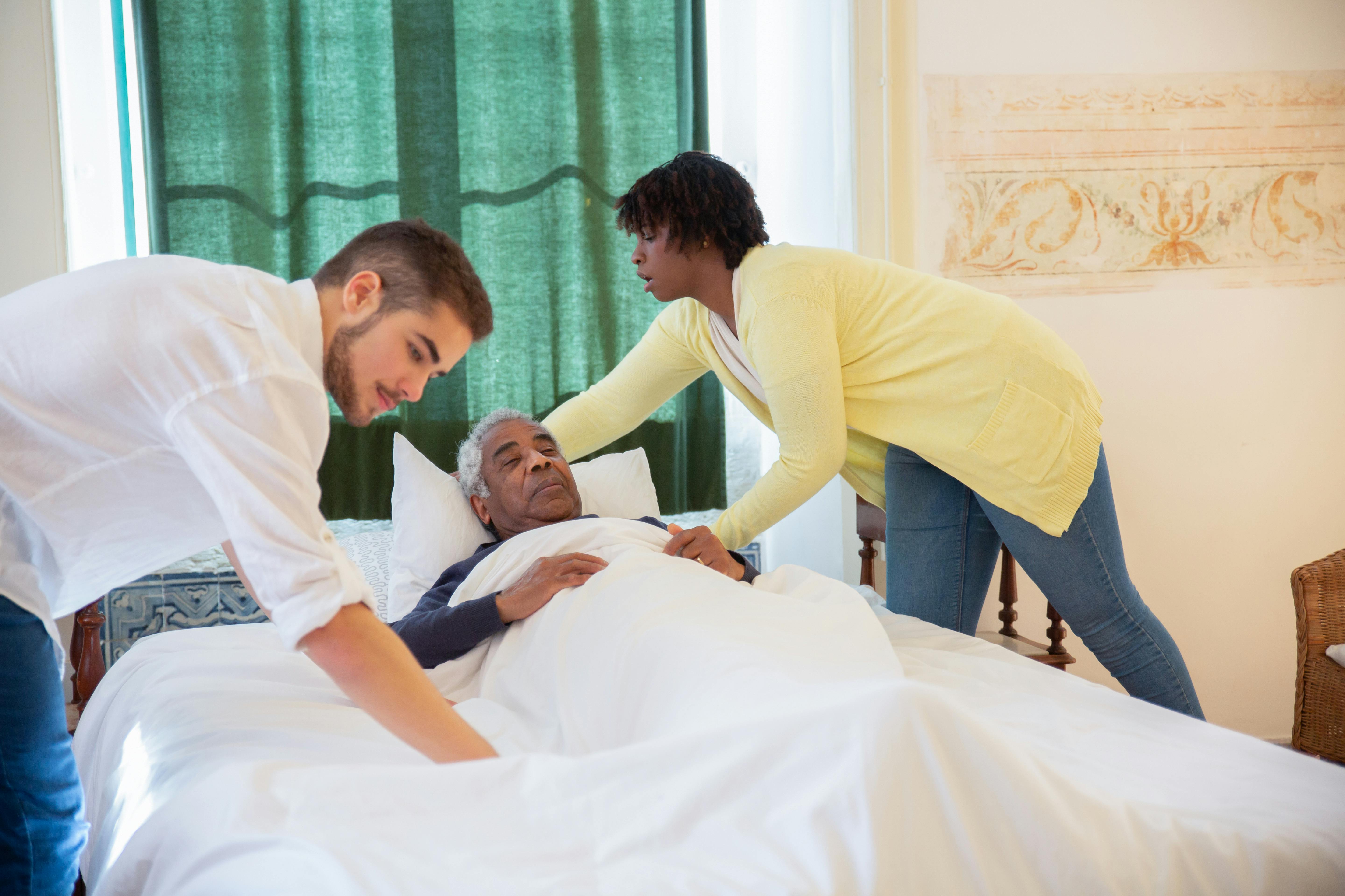 Two caregivers attentively caring for an elderly man at home